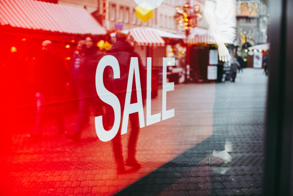 pexels-photo-3806753-3806753 Red sale sign on storefront window reflecting a busy urban street scene, capturing city life.