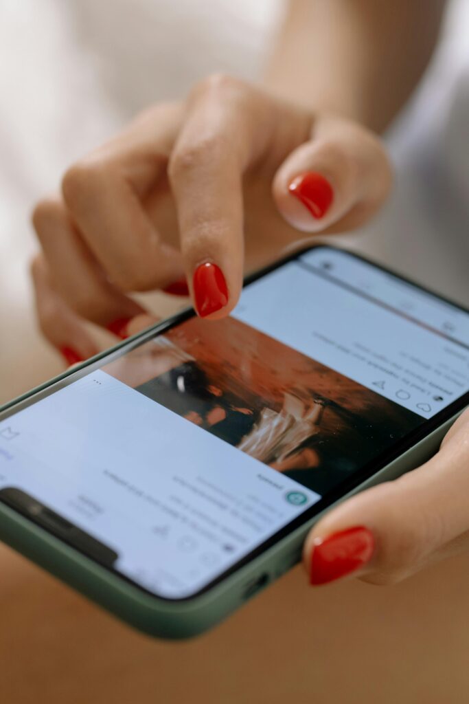 pexels-photo-6963589-6963589 A woman with red nails using a smartphone, navigating a social media app.